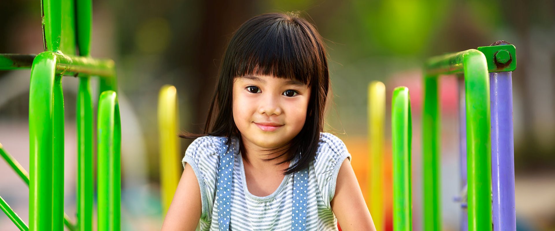 Little asian girl sitting on slide at playground